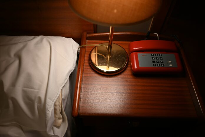 Wooden nightstand with a brass lamp and a red phone on it
